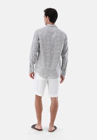 Camicia a maniche lunghe grigia con motivo paisley, abbinata a pantaloni corti bianchi, vista dal retro. Tessuto di cotone, colletto con bottoni e vestibilità comoda.