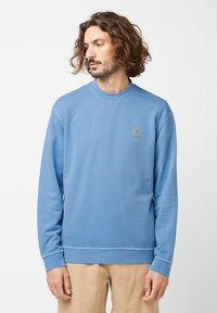 Lichte blauwe pullover sweatshirt met een geribde ronde hals en lange mouwen. Opvallend geborduurd logo op de borst in het groen. Gladde textuur.