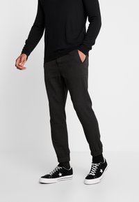 Tummanharmaat kapenevat housut, joissa on sivutaskut, yhdistettynä mustiin lenkkareihin, joissa on valkoisia tähtiä. Kevyt kangas, jossa on sileä rakenne.