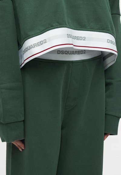 Πράσινη crop top με μακριά μανίκια και αντίστοιχο παντελόνι με λευκή και κόκκινη ρίγα στο τελείωμα, με το λογότυπο "DSQUARED2" σε γκρι κείμενο.