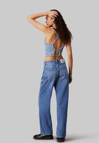 Top corto de mezclilla con un detalle en forma de ojal y tirantes finos, combinado con jeans de mezclilla azul de cintura alta y corte holgado, y zapatos de plataforma negros.