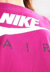 Fialový bavlněný top s velkým bílým logem "Nike" a designem swoosh, pod ním černé písmo "AIR".