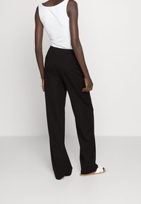 Czarne spodnie o szerokich nogawkach z gładką teksturą, z talią na wysokości środka oraz dwoma tylnymi kieszeniami. Połączone z prostym białym topem na ramiączkach.