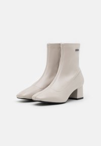 Stivali ankle in pelle beige con punta appuntita e tacco a blocco. Presentano una cerniera laterale e dettagli di cucitura minimali per un design elegante.
