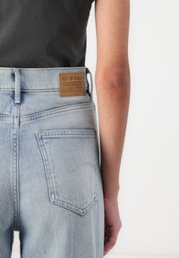 Jeans din denim de culoare albastru deschis cu talie înaltă, având un eticheta din piele maro G-Star Originals și buzunare de spate tradiționale.