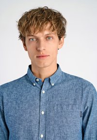 Lichtblauw overhemd met knoopsluiting van een gestructureerde stof, spread collar en een borstzak. Voorzien van witte knopen en een klein label aan de zijkant.