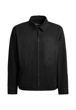 Sort lynlåstrøje med krave, lange ærmer, to forlommer og et diskret logo på venstre bryst, vist på hvid baggrund.