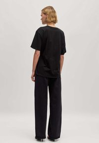 Zwarte katoenen t-shirt met een ontspannen pasvorm, korte mouwen en een ronde halslijn, gecombineerd met wijde donkerdenim broek.