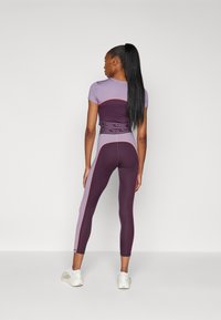 Lila és bordó sportöltözet, melynek része egy testhez simuló felső és leggings, oldalpanel díszítéssel rózsaszínben. Simagyűrő anyag és elasztikus derékpánt.