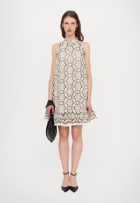 Spitzen-Halterkleid mit einem schwarzen und cremefarbenen, kunstvollen Muster, ausgestelltem Saum und gewellten Kanten; kombiniert mit einer schwarzen Clutch und hohen Schuhen.