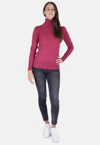 Pullover a collo alto magenta attillato, con texture a coste, maniche lunghe, abbinato a jeans skinny scuri e sneaker bianche. Design semplice senza motivi.