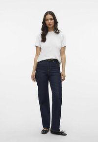 T-shirt blanc à manches courtes, jeans droit bleu foncé, chaussures plates noires. Tissu lisse, chemise ajustée, ceinture à la taille, quincaillerie minimale.