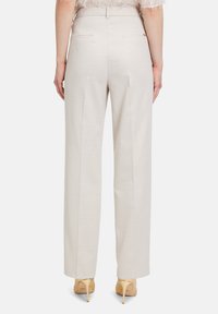 Lichtbeige tailleurbroek met een subtiele glans, recht gesneden ontwerp en twee achterzakken. Draag het met lichtgekleurde hakken.