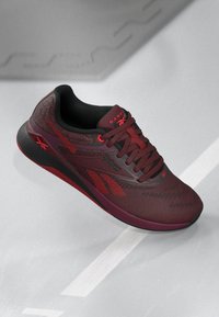 Maroon athletic shoe with mesh upper, textured pattern, and black accents. Features thick sole and contrasting laces. Logo on side.