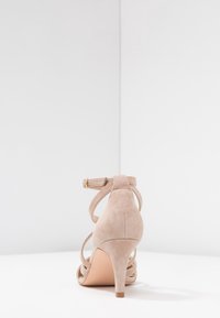 Sandali alti in suede beige con cinturino alla caviglia, dotati di fasce incrociate e tacco a stiletto sottile. Finitura con superficie liscia.