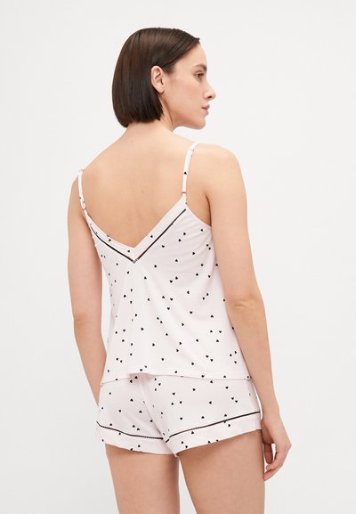 Svijetloružasti komplet za spavanje koji se sastoji od majice bez rukava i kratkih hlača, ukrašen malim crnim printovima u obliku srca i kontrastnim crnim detaljima.