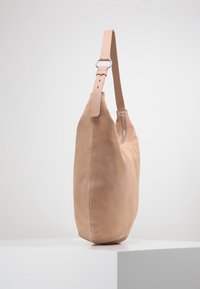 Měkká béžová semišová kabelka se strukturovaným tvarem, vybavená jedním nastavitelným popruhem a postranním zipovým uzávěrem. Hladký povrch.