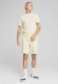 Lys gulstribet t-shirt og matchende shorts med et diskret logo. Bæres med hvide sokker og sneakers med sorte accenter.