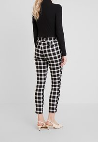 Pantalons à carreaux noir et blanc à coupe slim, taille haute avec poches arrière, associés à des chaussures à talons de couleur claire.