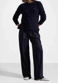 Laivastonsininen palmikkoneule, jossa on resorit helmassa ja hihoissa, yhdistetty korkeavyötäröisiin, leveälahkeisiin tummiin housuihin ja vaaleanvärisiin tasapohjaisiin kenkiin.