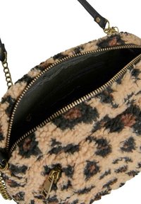Bolso redondo hecho de tela de felpa con un patrón de leopardo en tonos beige, negro y marrón. Presenta una cremallera dorada y un interior negro.