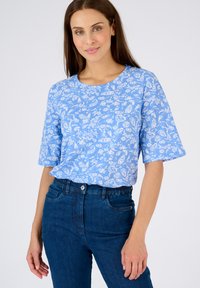 Top corto de manga corta con estampado floral azul en tela ligera, combinado con jeans azul oscuro que cuentan con una cinturilla elástica y un corte clásico.