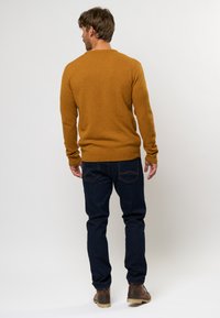 Brauner Strickpullover mit rundem Halsausschnitt, kombiniert mit dunkelblauer Jeans und braunen Schuhen. Die Textur wirkt weich und gemütlich.