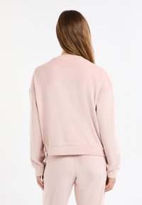 Sudadera rosa claro con textura acanalada, corte holgado, hombros caídos y dobladillo cropped. Textura suave, diseño minimalista, sin elementos metálicos visibles.