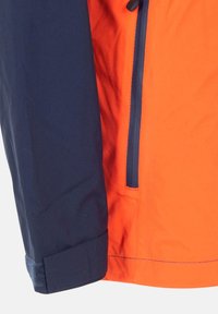 Färgbockad jacka med en marinblå vänsterärm och en lysande orange kropp, med en dragkedjeficka och kardborreband vid ärmsluten.