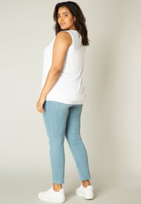 Witte mouwloze top gecombineerd met lichtblauwe skinny jeans en witte sneakers. De jeans hebben een raw-hem detail voor extra textuur.
