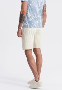 Shorts bianchi di cotone con una texture liscia, dotati di una vita elasticizzata. Indossati con una camicia a maniche corte, a fiori, di colore azzurro chiaro.