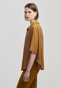 Korte mouwen, kraagloos shirt in mosterdgeel, met een losse pasvorm en textuurstof, gecombineerd met bijpassende mosterdkleurige broek.