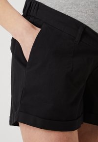 Svarte shorts med en avslappet passform, kjennetegnet av en rullet kant, sidelommer og en elastisk midje for komfort. Laget av et glatt stoff.