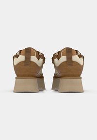 Brune semskede sneakers med cremefarvede accenter, der har en rem ved hælen, struktureret overflade og en tykk beige sål.