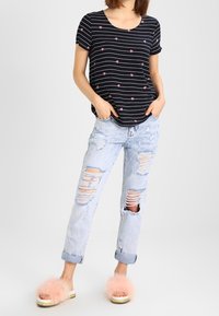 T-shirt rayé noir et blanc avec des accents floraux roses, jean bleu clair déchiré, et sandales slides roses duveteuses avec un accent doré.