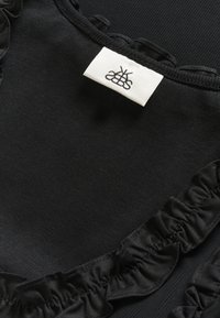 Black top featuring a textured fabric with a ribbed design. A ruffled trim accents the neckline. Care label included.
