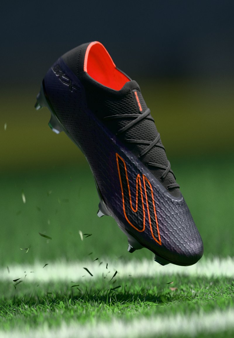 Scarpino da calcio nero con accenti arancioni, tomaia texturizzata e lacci neri, caratterizzato da un design curvo e tacchetti, catturato in aria sopra l'erba.