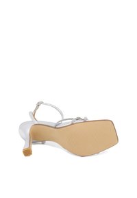 Sandali argentati con tacco alto e punta aperta, dotati di una sottile cinghia alla caviglia e decorati con perline. La suola è beige con scanalature testurizzate.