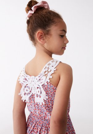 Vestido con estampado floral en rosa, rojo y azul, que presenta un diseño de mariposa de encaje blanco en la parte posterior con acentos de pompones. Tirantes ajustables.
