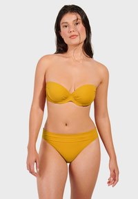 Žuti bikini set s bez naramenica gornjim dijelom s nabranim čašicama i gaćicama visokog struka s glatkim pojasom. Izrađen od rastezljivog, laganog materijala.