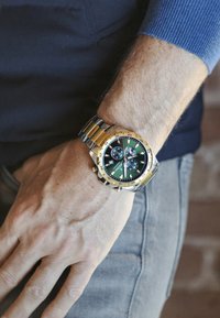 Zelta un sudraba rokas pulkstenis ar zaļu ciparnīcu, trim subciparnīcām un melniem akcentiem, ar metāla saiti.