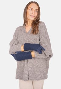 Marineblaue gestrickte Handschuhe mit gerippten Bündchen, die über einem gemütlichen grauen Pullover getragen werden. Die Handschuhe haben eine nahtlose, weiche Textur und passen eng.