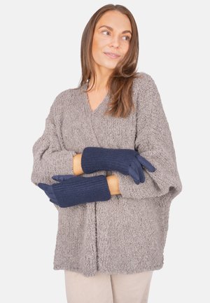 Marineblaue gestrickte Handschuhe mit gerippten Bündchen, die über einem gemütlichen grauen Pullover getragen werden. Die Handschuhe haben eine nahtlose, weiche Textur und passen eng.