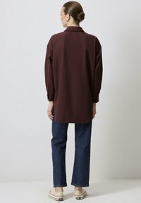 Vinröd långärmad skjorta med krage, avslappnad passform och sidoklor, kombinerad med mörkblå raka jeans och beige sneakers.