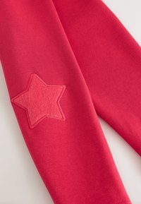 Red cotton leggings featuring a textured pink star patch on the knee, with smooth fabric and a fitted design.