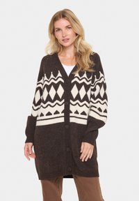 Brun oversized cardigan med krämfärgade geometriska mönster, knapplist fram och ribbade ärmslut. Tillverkad av mjuk ullblandning för värme och komfort.