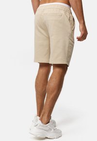 Beige denim shorts med elastisk talje, sidelommer og en afslappet pasform. Bagudvinklen viser tvilling baglommer og pæne syninger.
