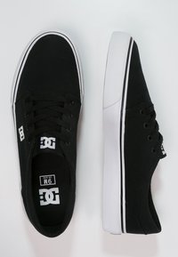 Black canvas sneakers with white rubber soles, featuring round laces, a logo on the side, and a simple low-top design.