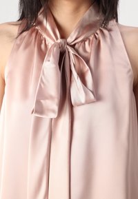 Blusa di seta rosa pallido con un fiocco legato al colletto. Presenta dettagli arricciati e una texture liscia e fluida.