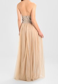 Stropplös klänning med en åtsittande, glittrande överdel och en flödande beige tyllkjol, med dragkedja i ryggen och lagerstruktur för volym.